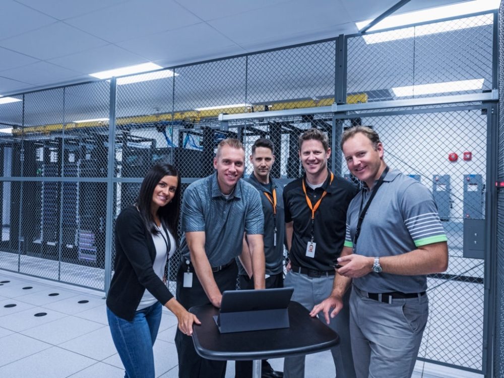 managed security service team standing in front of a bunch of servers in a data center smiling