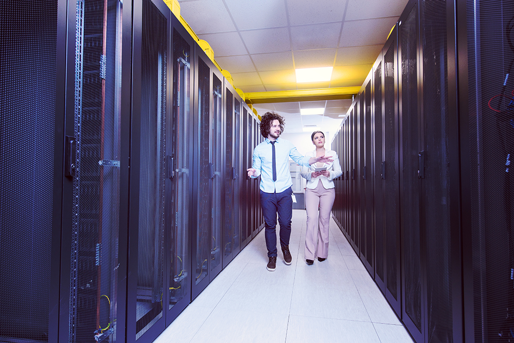 Young IT engineer showing working data center server room to female chief engineer who holding tablet computer