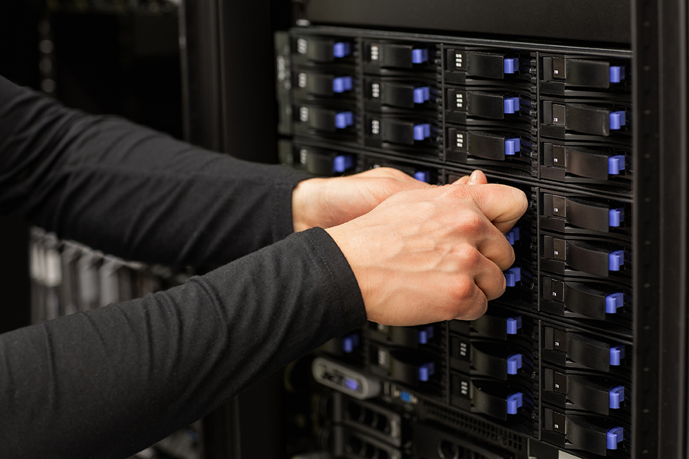 Cropped hands of male technical consultant adjusting hard drives stack in SAN at datacenter