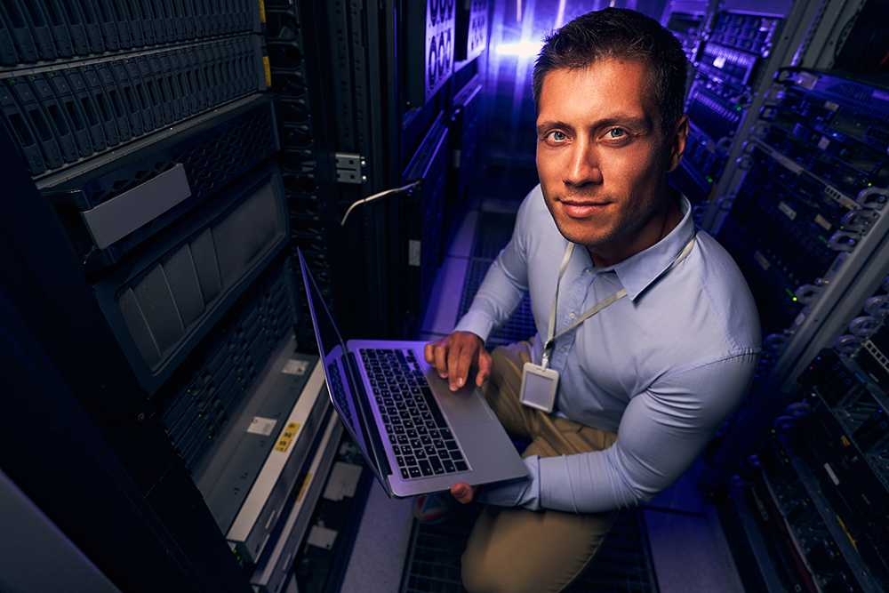 Serene system administrator with laptop sitting on his haunches in server room