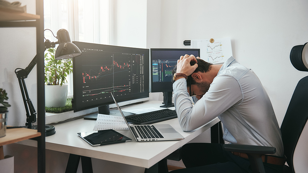 Feeling sad. Depressed young businessman or trader in formalwear keeping head in hands while working in the office. Computer screens with trading charts and financial data. Stock exchange. Financial trading concept. Investment concept