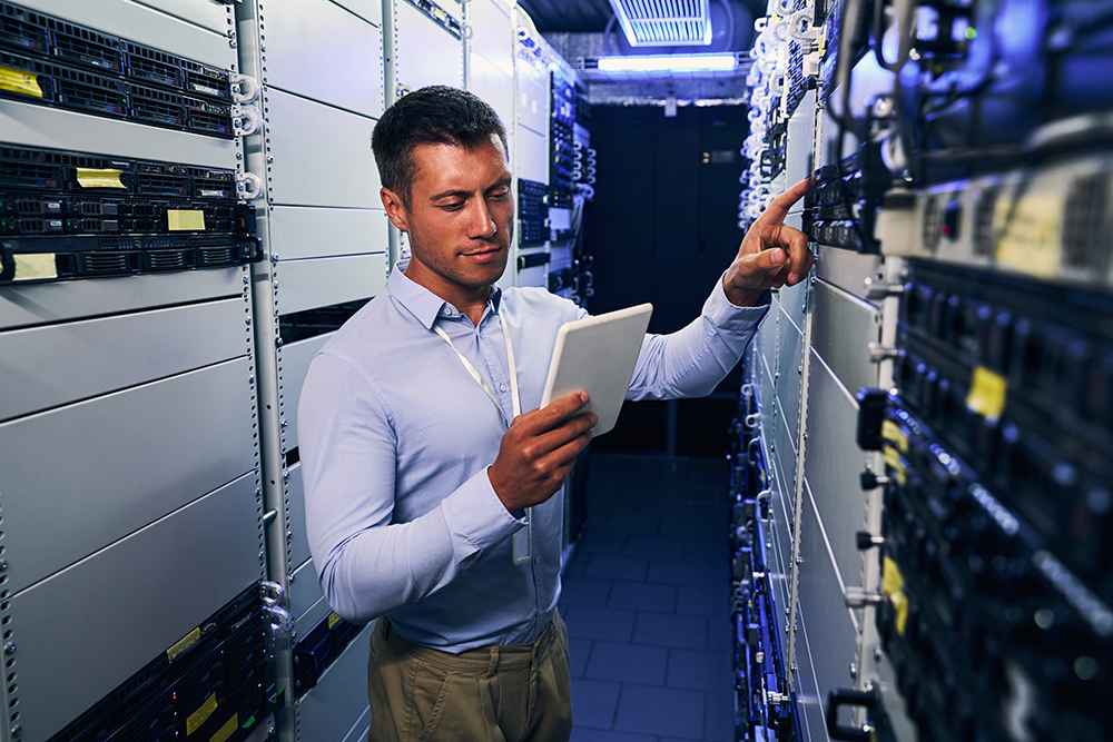 Focused serious male engineer checking networking equipment in data center