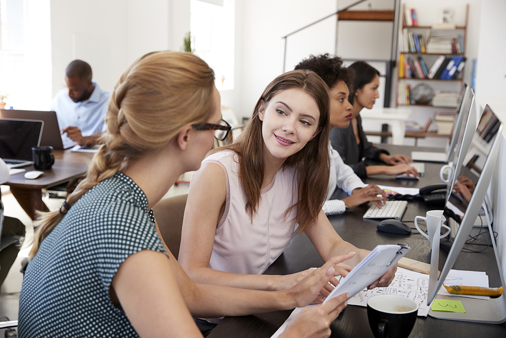 Woman training new female employee in an open plan office