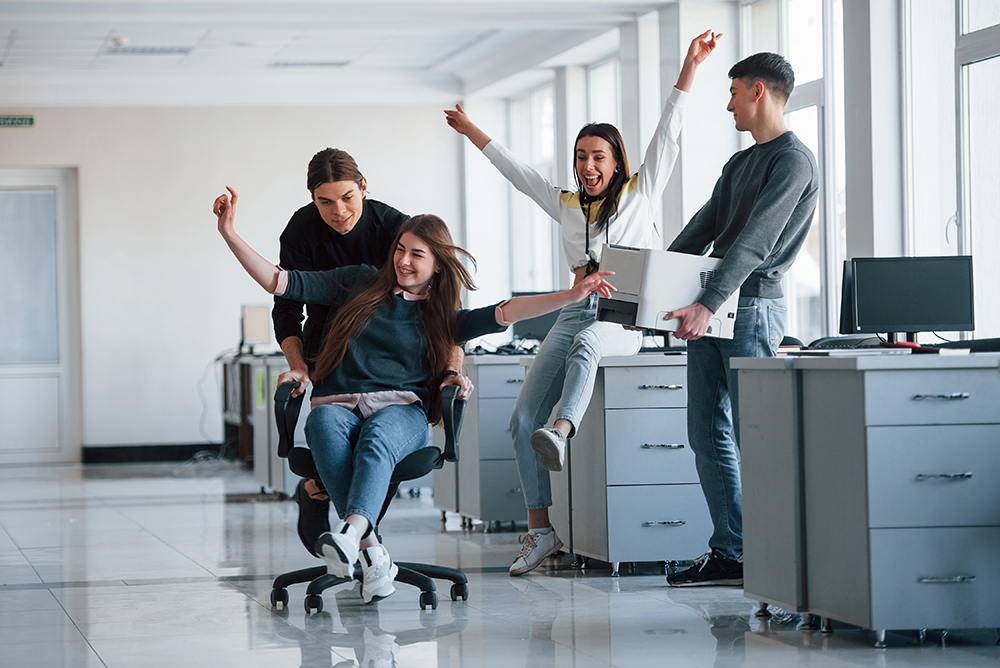 Man holds printer. Having fun in the office. Young people have a break and driving by using a seat.