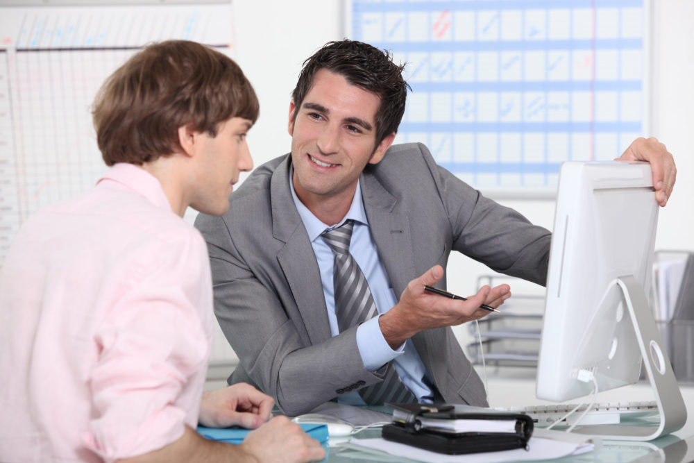 Manger talking to a young staffer member while staring at a computer monitor