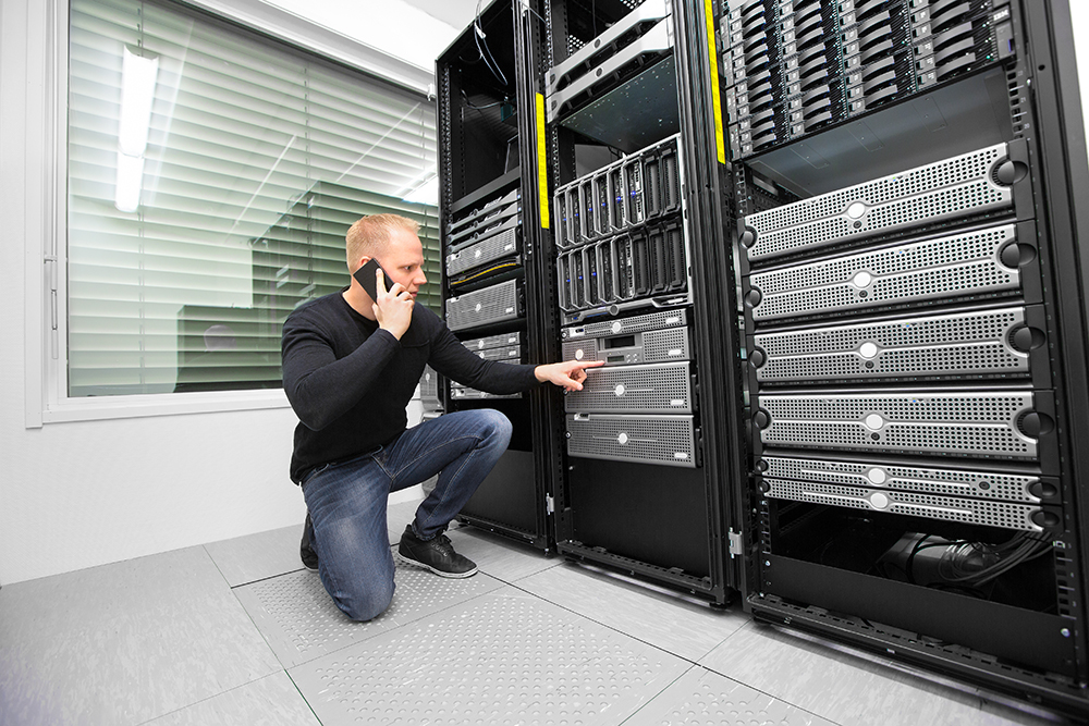 Full length of IT consultant using smartphone while monitoring servers in datacenter