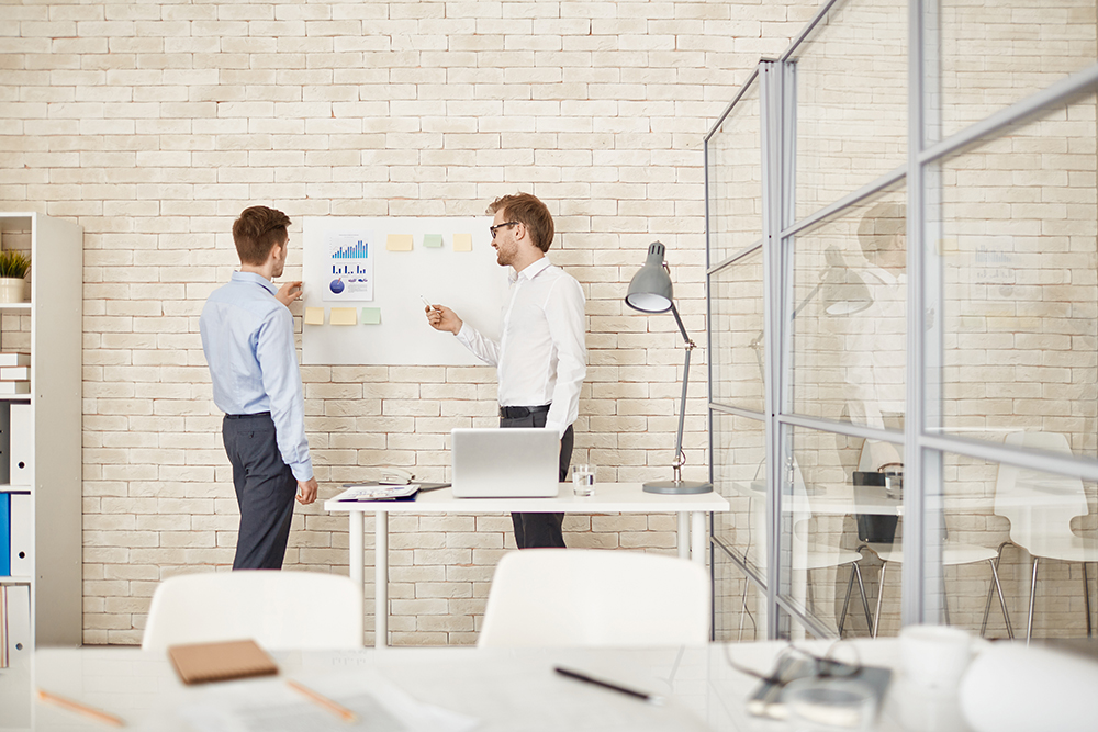 Young businessman pointing at document on board while explaining data to colleague