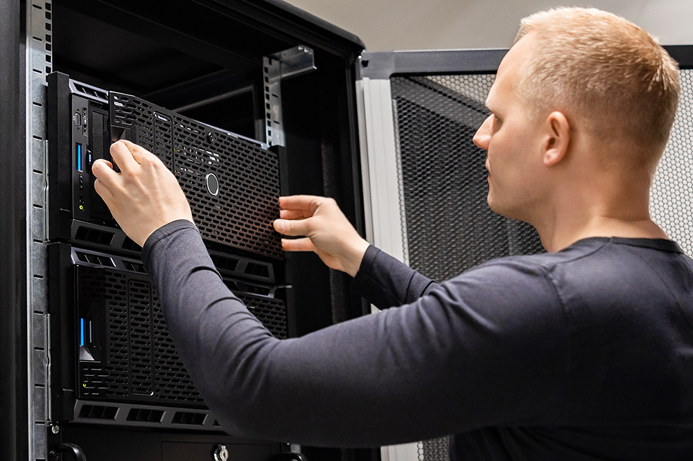 Confident male technician installing servers in enterprise datacenter for cloud hosting.