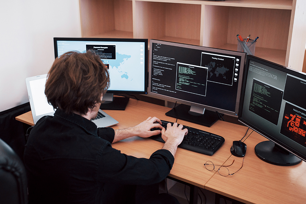 The young dangerous hacker breaks down government services by downloading sensitive data and activating viruses. A man uses a laptop computer with many monitors