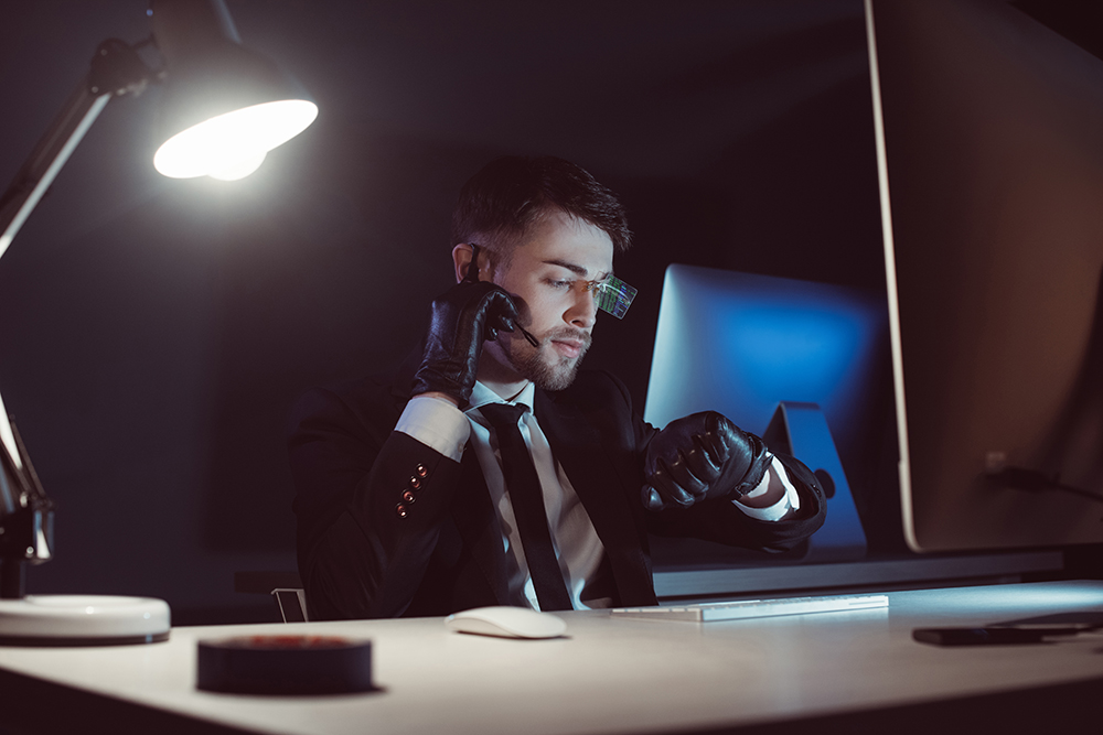 portrait of spy agent in gloves with headset checking time at table with computer screen in dark