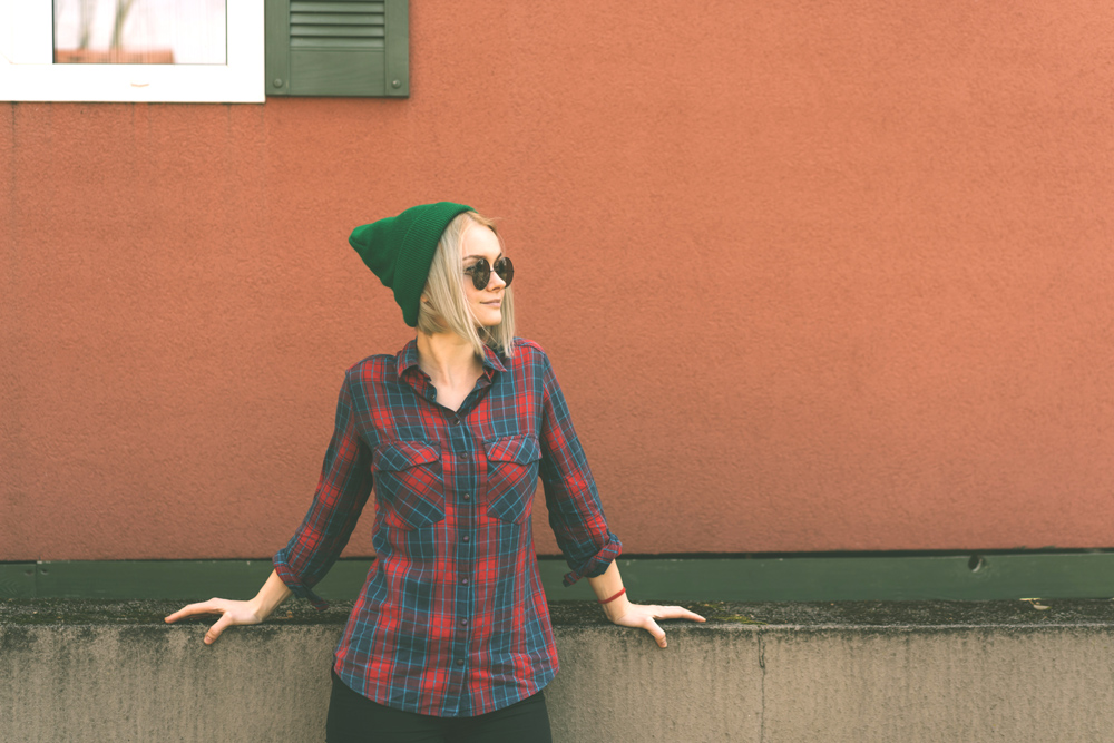 Blonde hipster girl in a plaid shirt in a green hat and sunglasses