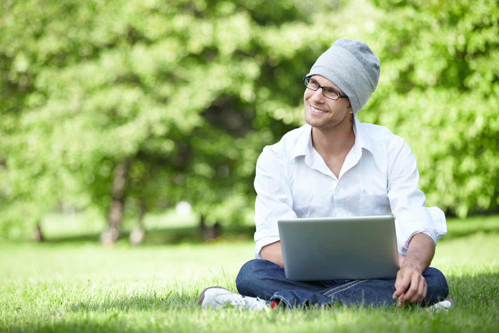 Attractive young man in a hat with a laptop outdoors