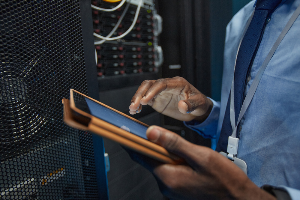 Close up of man holding digital tablet while standing by server cabinet and working with supercomputer in data center, copy space