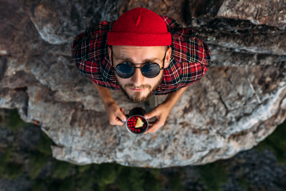 Portrait of a man in a red hat who stands against the background of mountains and looks at the camera. Portrait of a tourist. A traveling man in a plaid shirt against the background of mountains.