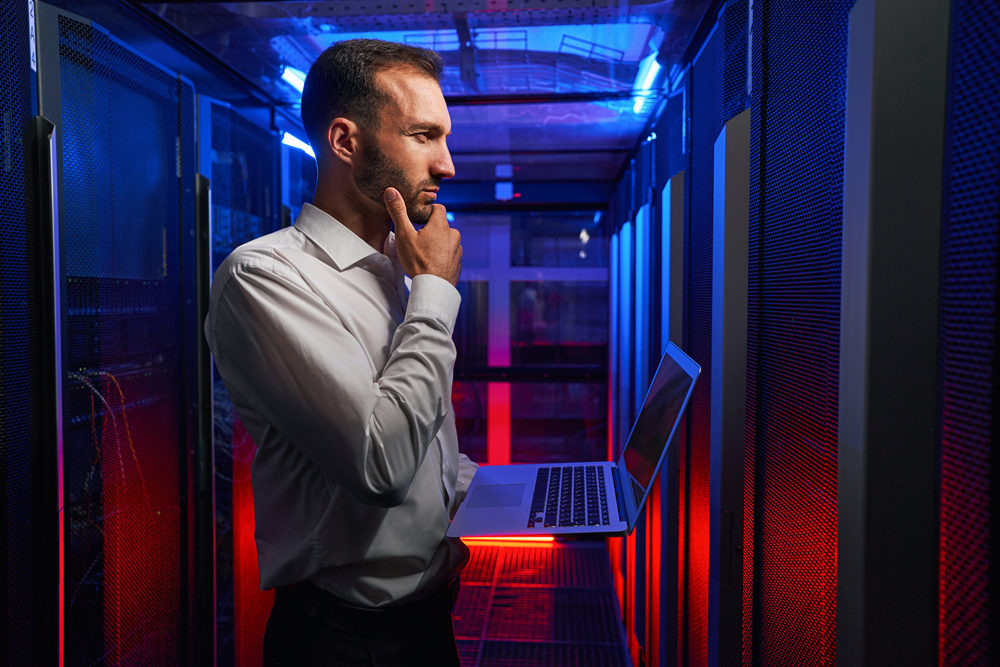 System administrator working on laptop while looking to the server rack