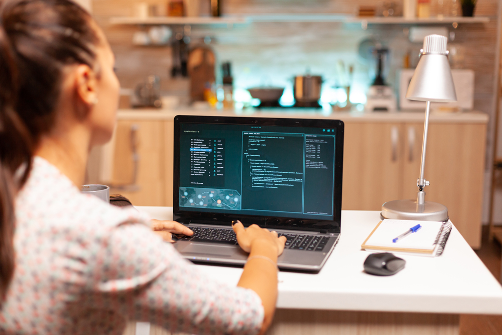 Woman doing cyberspace criminal activity hacking firewall using laptop from home office at night time. Programmer writing a dangerous malware for cyber attacks using performance laptop during midnight.