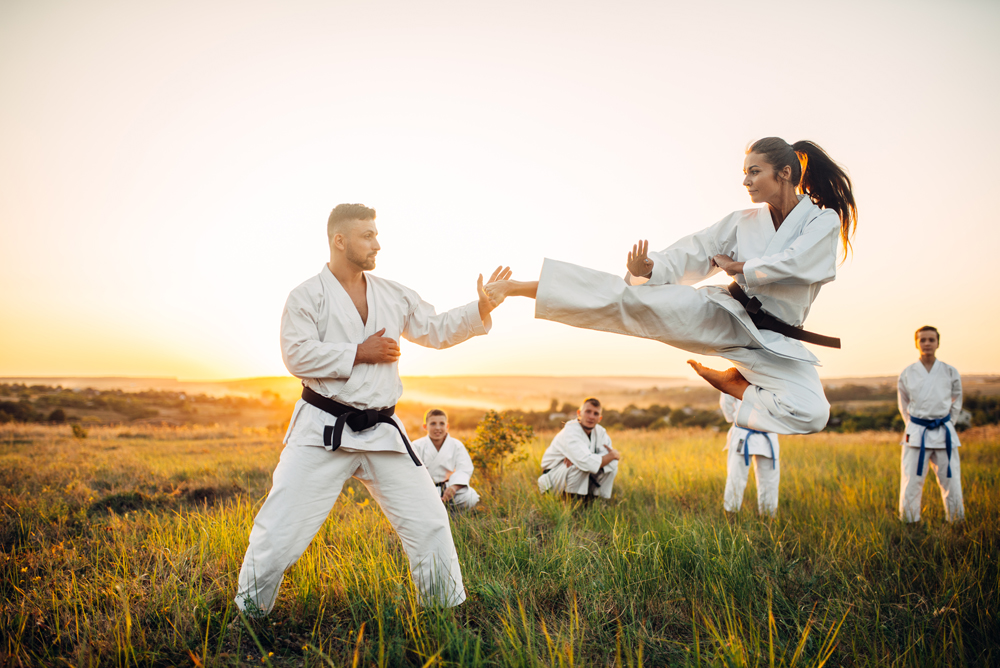 Female karate fighter trains kick in flight with master. Martial art fighters on workout outdoor, technique practice. Photo manipulation with background