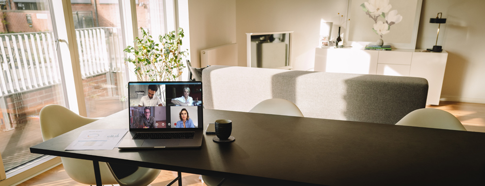 Hosted PBX For Small Business Laptop on table with a video call on the screen in living room. People using VoIP to connect together.