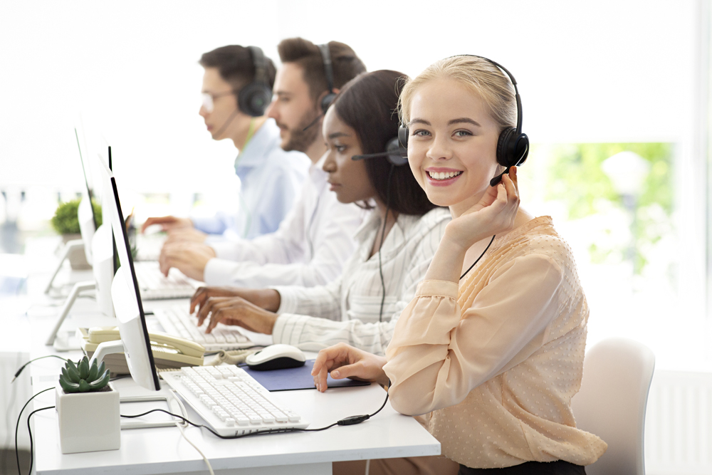 Team of diverse hotline operators with headphones providing service to clients at call center. Young customer support representatives working in telemarketing or telecommunications at modern office