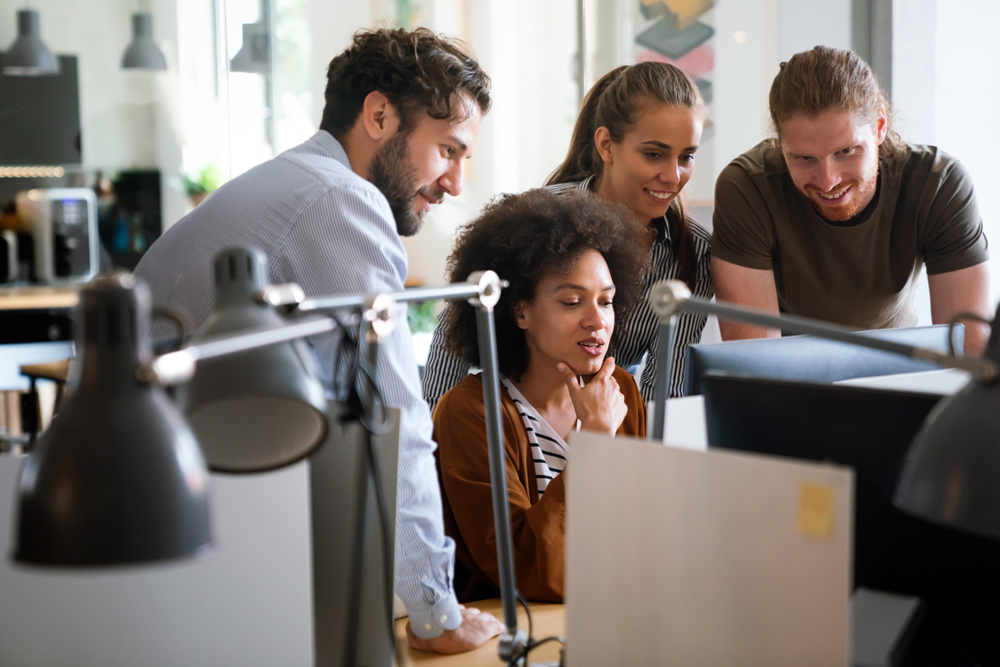 Diverse group of professionals meeting in office. IT programmers use computer, talk strategy. Specialists create innovative software. Engineers develop inspirational app