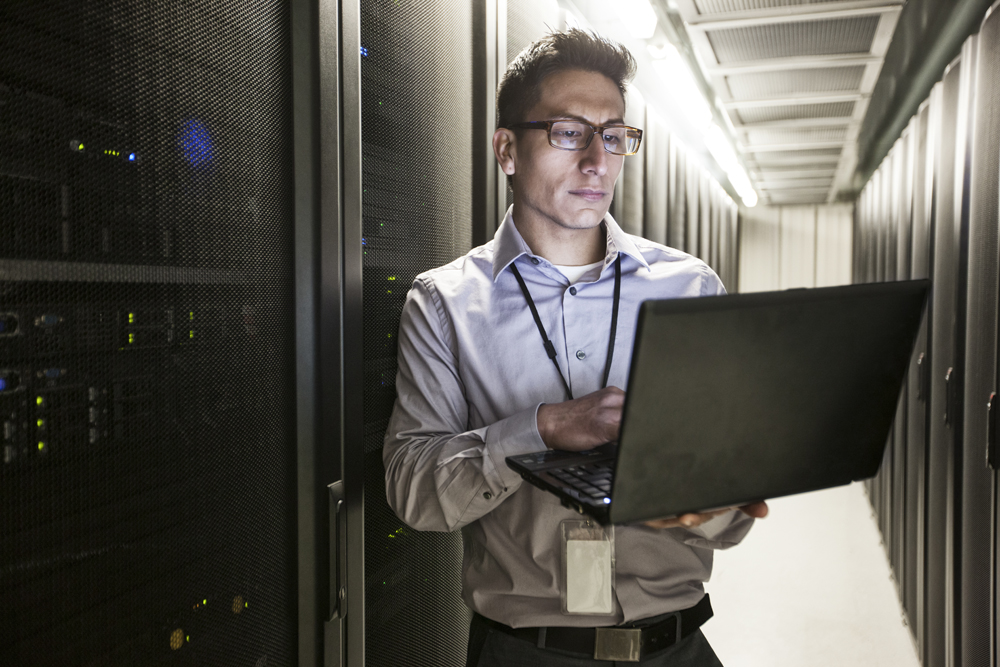 Hispanic man technician doing diagnostic tests on computer servers in a large server farm.