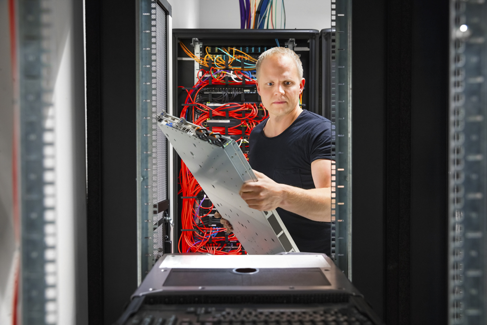 Confident male IT engineer mounting and installing server at datacenter