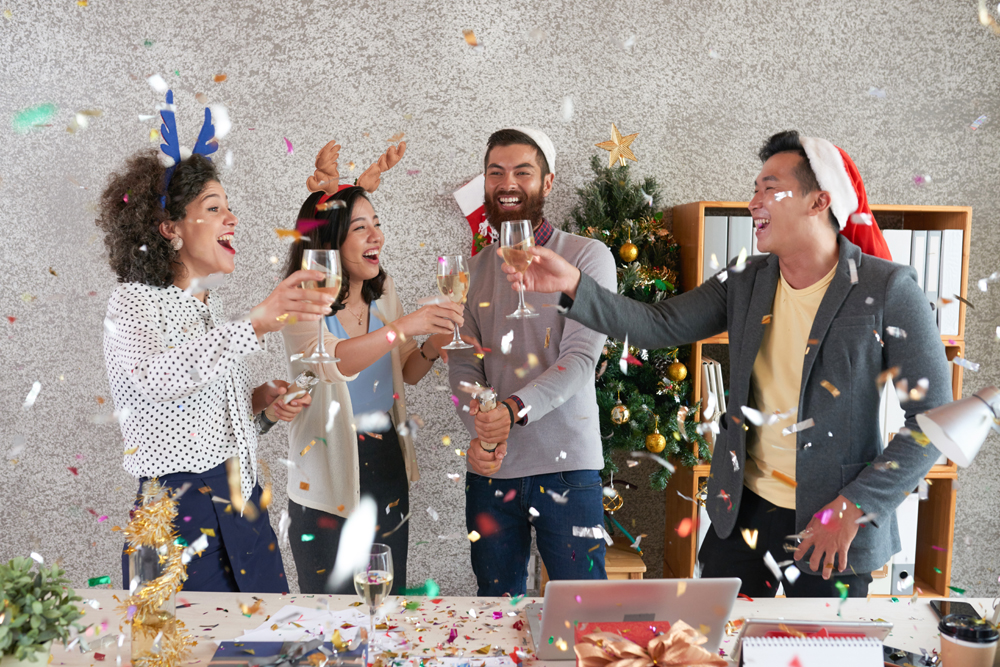 These people are celebrating because they followed our holiday cybersecurity tips. Group of joyful young coworker enjoying New Year celebration in office. They are toasting under confetti rain