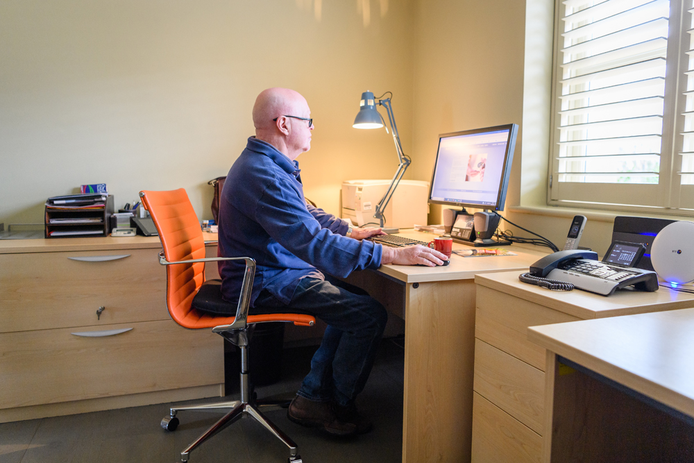 Old man working from home on a computer sitting in an orange rolly chair
