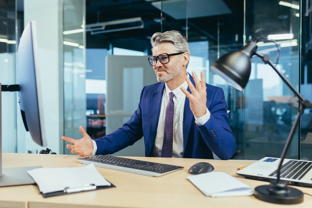 Angry and upset boss businessman shouting at computer monitor, man with glasses working in modern office at computer