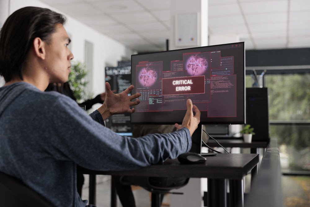 Nervous app developer having system error message on computer screen, trying to solve hacking alert problem. System engineer looking at hacked server on pc monitor in it office room.