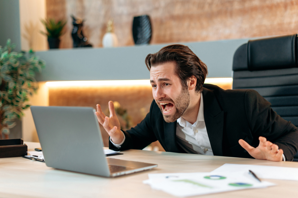 Shocked annoyed angry caucasian business man, stock trader, product manager, working in a modern office, yelling to the laptop, frustrated by the disruption of his wifi network while making an important deal