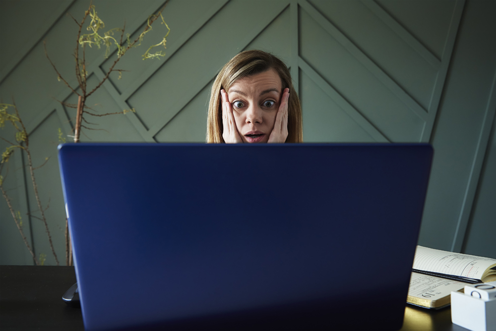 Shocked woman looking at laptop screen with rounding eyes. Her system has crashed and she hasn't read our IT problems and solutions blog post.