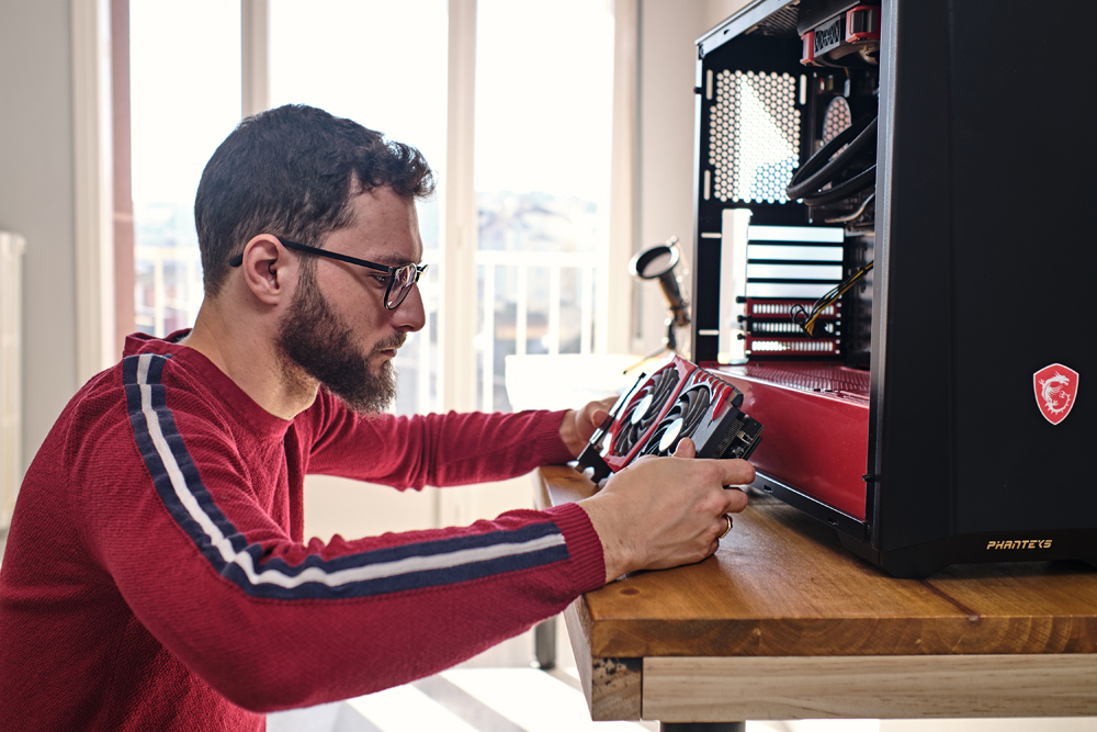 Side view of an adult man holding and looking at graphics card near his cpu tower.