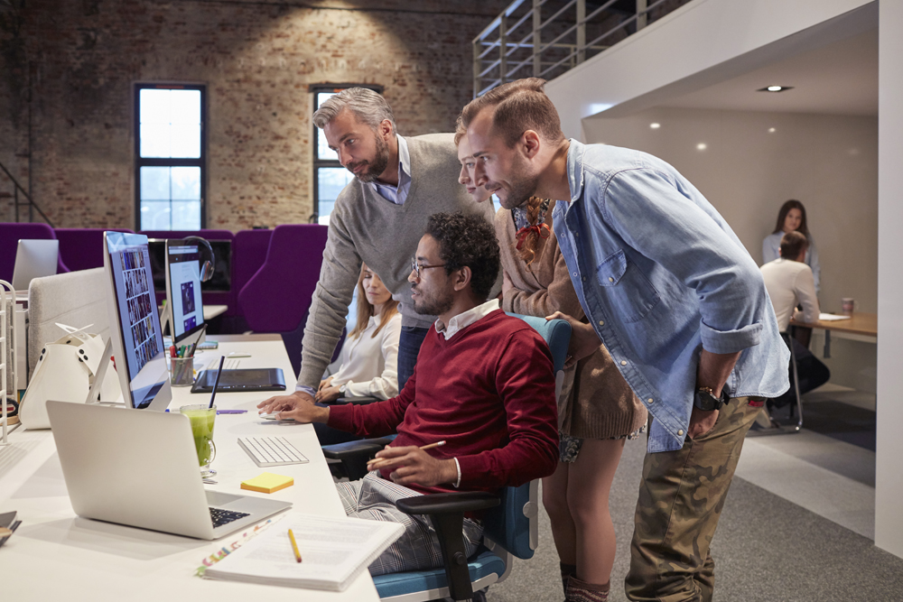 Two men shoulder surfing their colleague. 