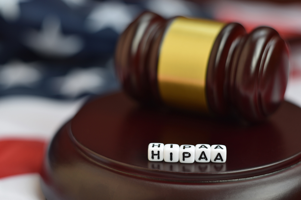 A gavel with the letters HIPAA on blocks in front of it with an American flag in the background
