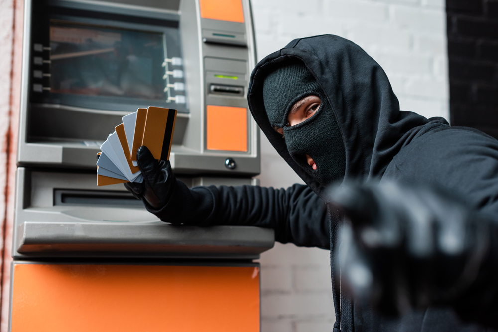 A thief in front of an atm holding up many peopple's debit cards