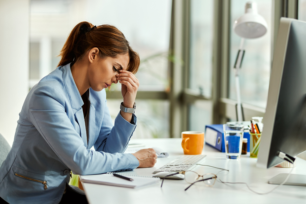 Young businesswoman suffering from MFA fatigue holding her head in pain while working in the office.