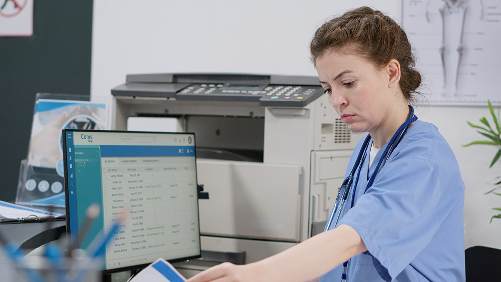 Nurse using computer with appointments at reception desk in facility lobby, working on report papers with healthcare insurance. Medical assistant doing registration support at hospital center.