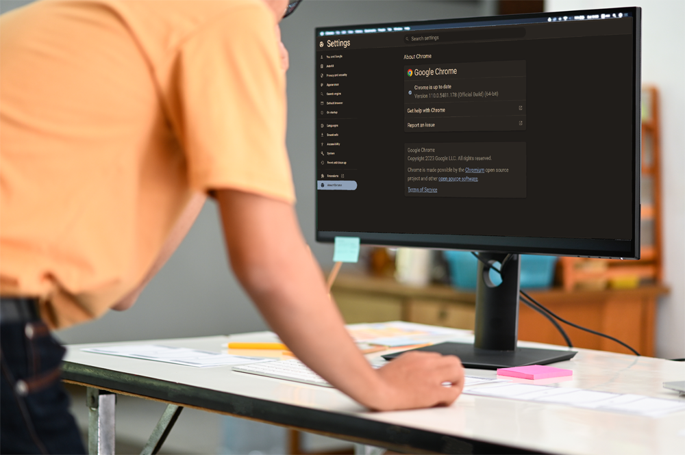 A young employee is standing in front of his desk holding a mouse and looking at a computer monitor that just updated Google Chrome