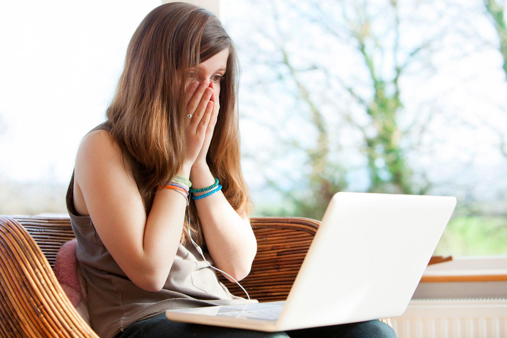 A woman holding her face staring at her laptop after she had been hacked