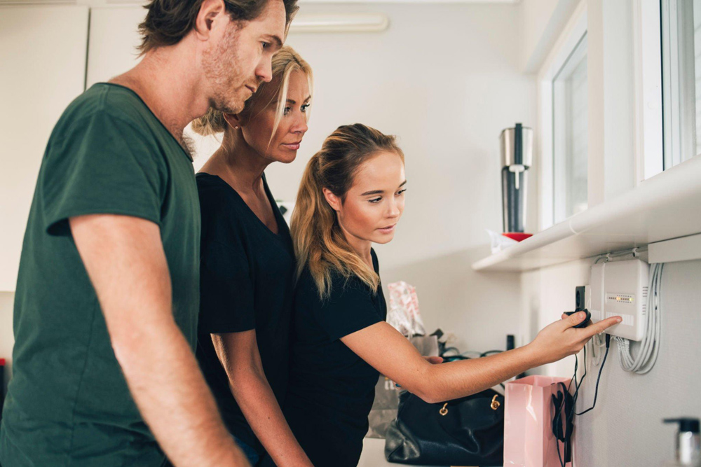 A woman and two colleagues resetting a white router in an office