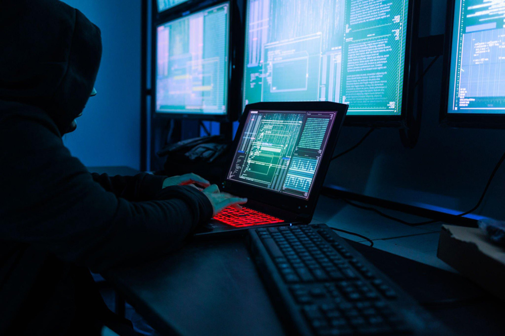 Hacker in a dark room surrounded by computer monitors