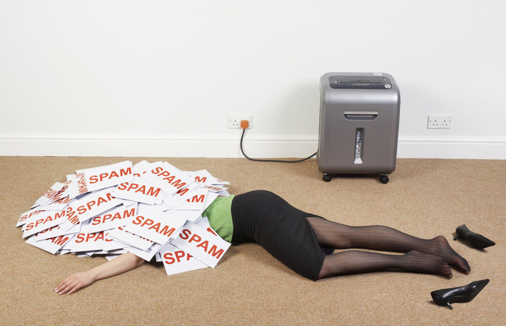 LAdy underneath a pile of spam emails by the paper shredder