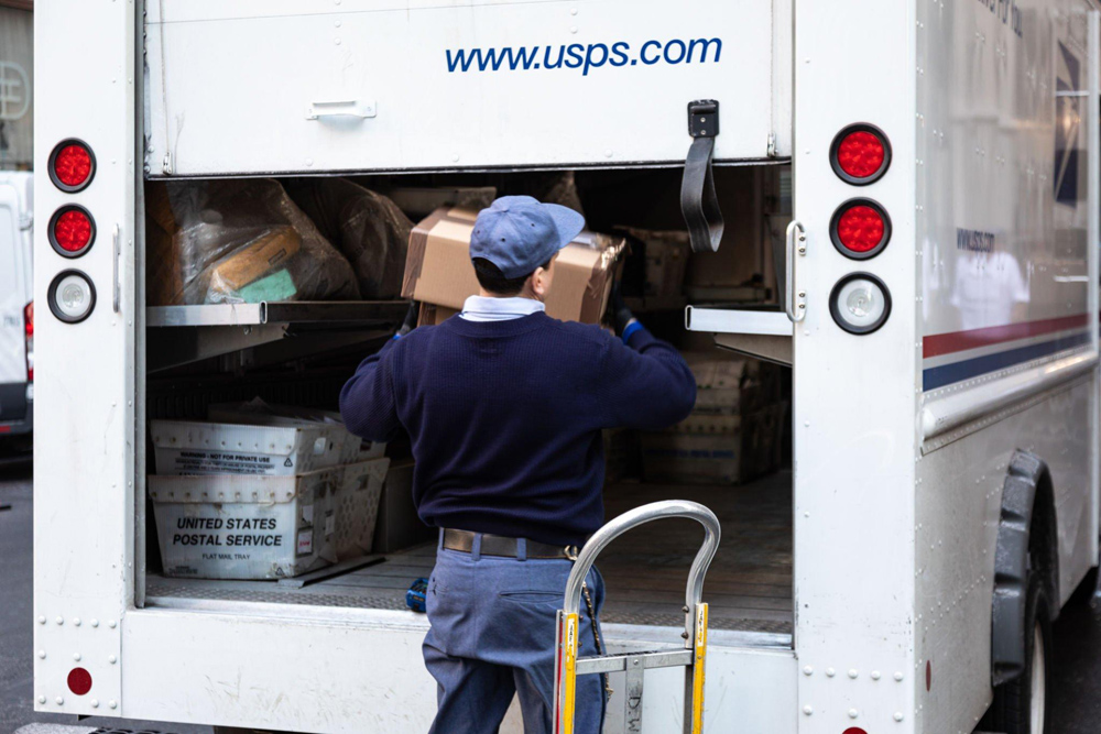 Mail carrier putting packages in the back of his truck. 